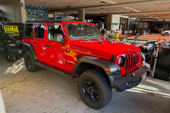 Red Jeep Wrangler parked on a street near rental signs.
