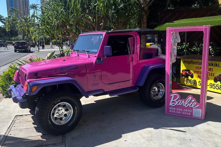 Pink Jeep with a Barbie-themed photo booth on a sunny street.