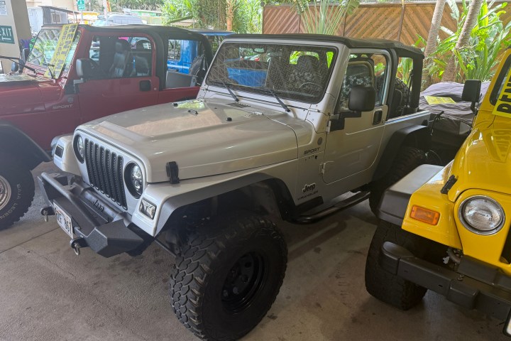 Silver Jeep Wrangler parked between red and yellow Jeeps.