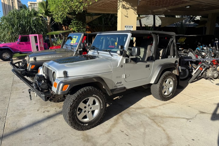 Silver Jeep with roof open, parked beside motorcycles and another vehicle.