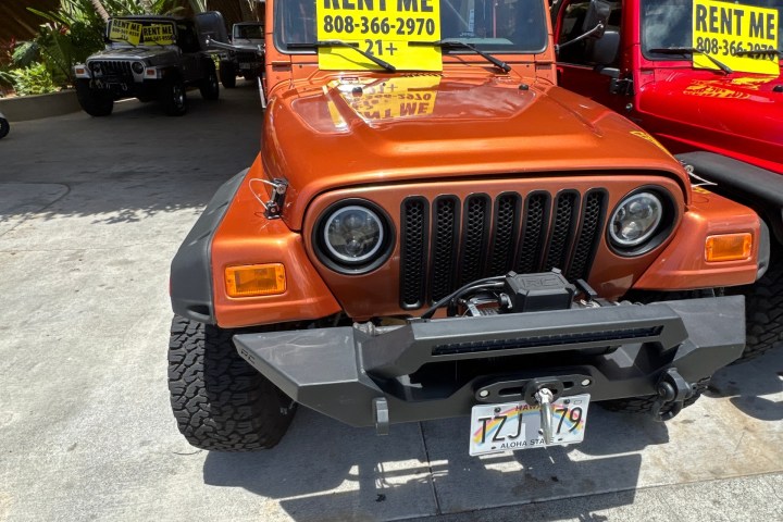 Orange Jeep for rent with sign, parked in lot with other vehicles.