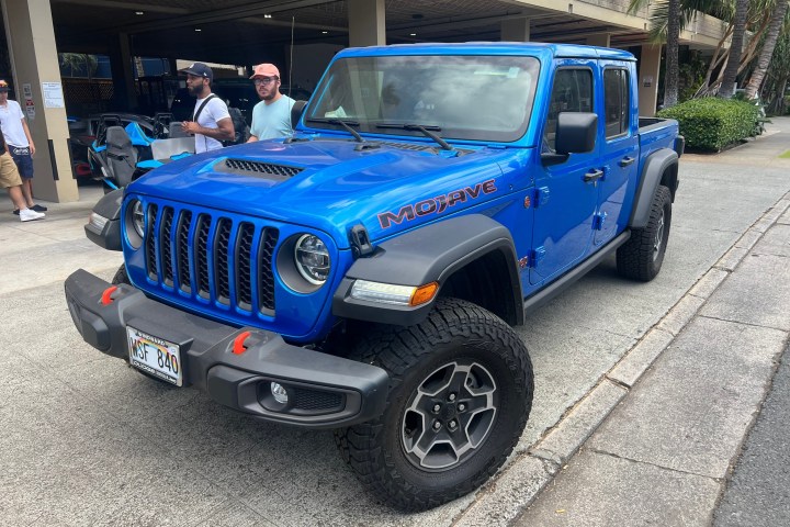 Blue Jeep Gladiator truck parked on a street with people nearby.