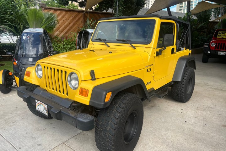 Yellow Jeep Wrangler parked outdoors with palm trees in the background.