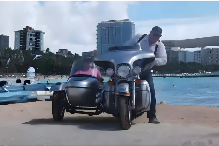 Motorcycle with sidecar on beach, two people, city skyline background.