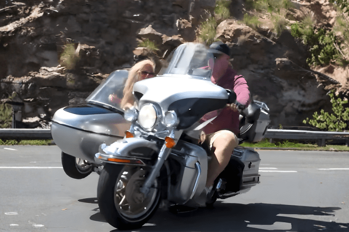 Man riding a motorcycle with a sidecar on a mountain road.